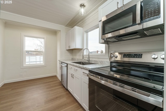 kitchen featuring appliances with stainless steel finishes, sink, white cabinets, light stone counters, and light hardwood / wood-style floors