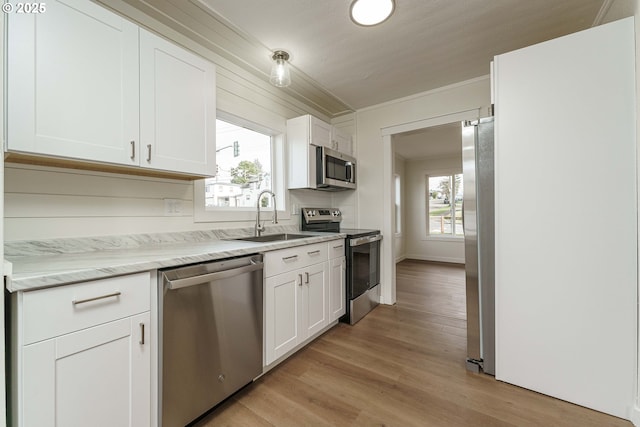 kitchen with sink, appliances with stainless steel finishes, light stone counters, light hardwood / wood-style floors, and white cabinets