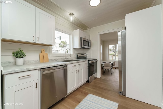 kitchen with appliances with stainless steel finishes, a wealth of natural light, sink, white cabinets, and light hardwood / wood-style floors