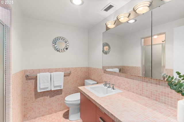 full bath with toilet, a stall shower, wainscoting, vanity, and tile walls