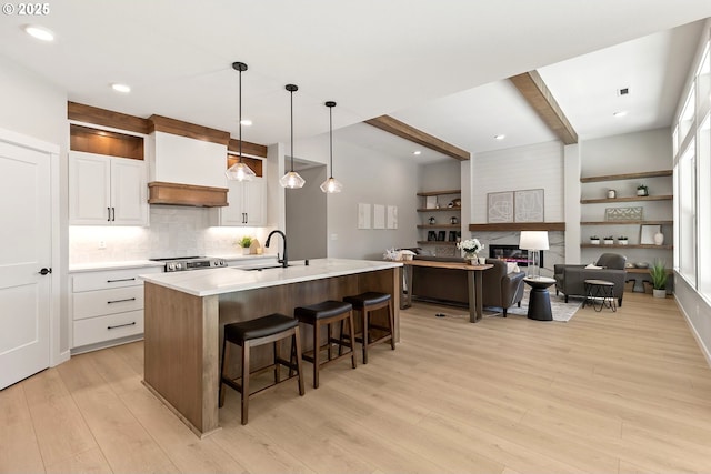 kitchen with beam ceiling, a sink, light countertops, white cabinets, and light wood-type flooring