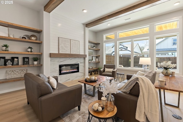 living room with beamed ceiling, built in shelves, wood finished floors, recessed lighting, and a premium fireplace