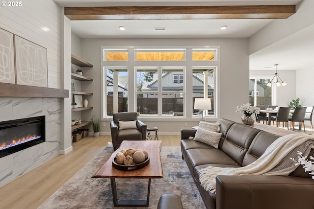 living room with beam ceiling, light wood finished floors, a premium fireplace, baseboards, and a chandelier