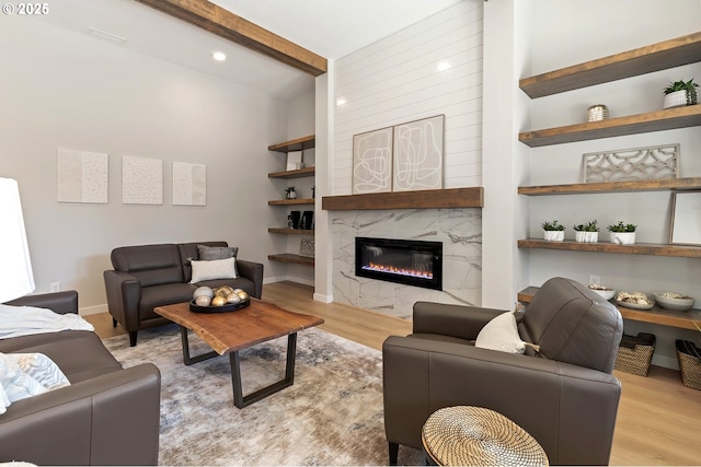 living area with a high end fireplace, beam ceiling, baseboards, and light wood finished floors