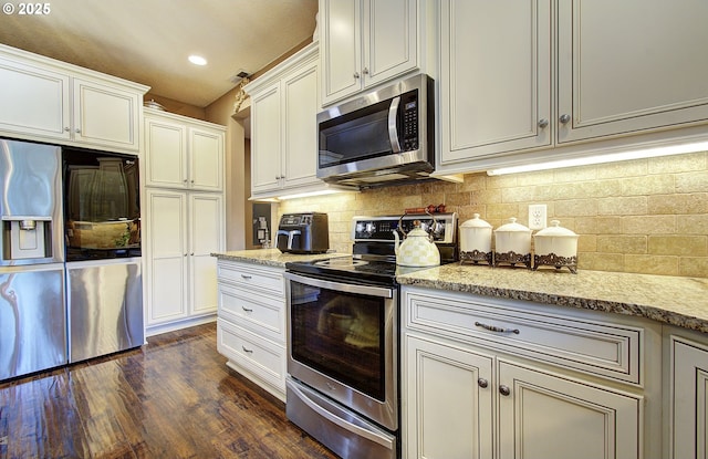 kitchen with dark wood-type flooring, appliances with stainless steel finishes, light stone countertops, decorative backsplash, and white cabinets