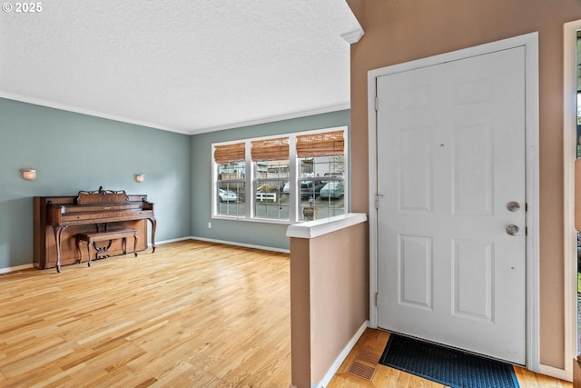 foyer featuring a textured ceiling, crown molding, baseboards, and wood finished floors