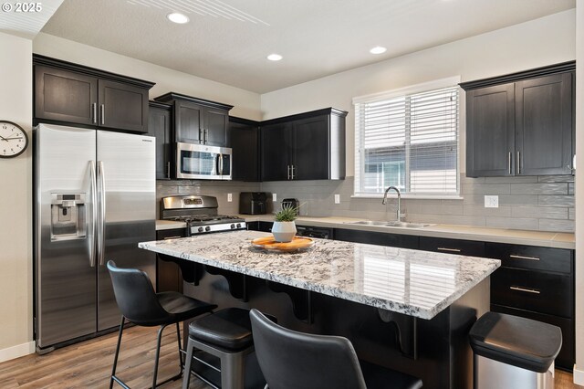14139 SW Burlwood Ln, Beaverton, OR 97005 - kitchen with appliances with stainless steel finishes, a kitchen island, light wood finished floors, a breakfast bar area, and tasteful backsplash