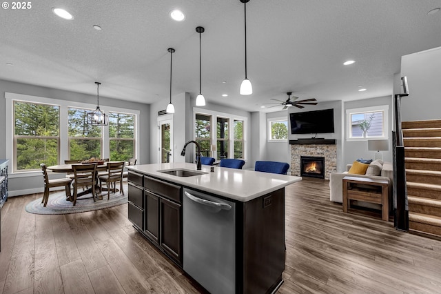 kitchen featuring dishwasher, a sink, a stone fireplace, light countertops, and ceiling fan