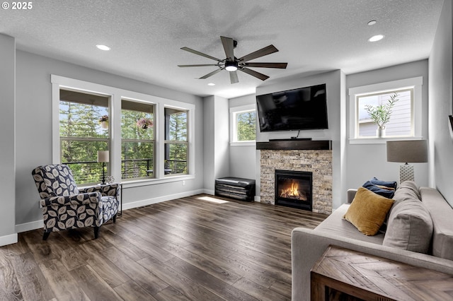 living room featuring a textured ceiling, ceiling fan, baseboards, recessed lighting, and a stone fireplace