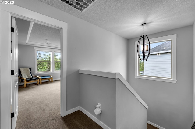 hallway with an upstairs landing, a textured ceiling, dark colored carpet, baseboards, and a chandelier