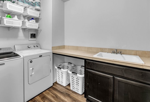 clothes washing area with independent washer and dryer, wood finished floors, and cabinet space