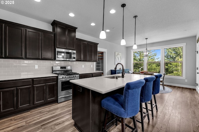 kitchen with appliances with stainless steel finishes, a sink, light wood-style flooring, a kitchen island with sink, and a textured ceiling