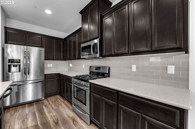 kitchen with appliances with stainless steel finishes, wood finished floors, light countertops, backsplash, and a textured ceiling