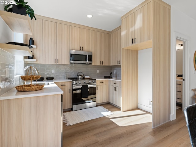 kitchen featuring appliances with stainless steel finishes, light brown cabinets, light wood-style floors, tasteful backsplash, and a sink