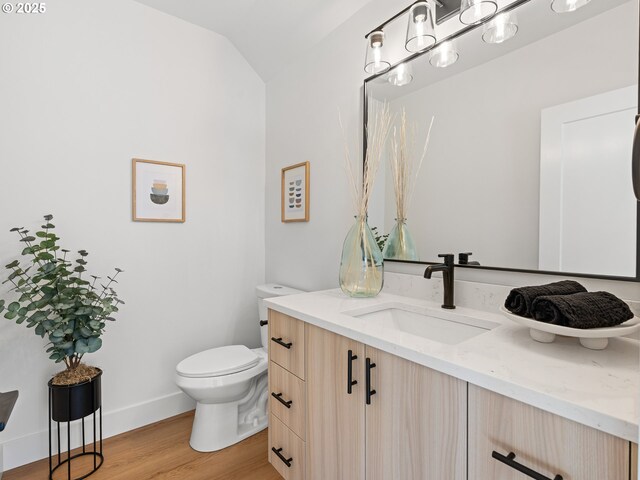half bath with toilet, wood finished floors, vanity, lofted ceiling, and baseboards