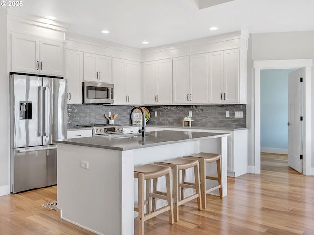 1155 SE Bugle Ave, Warrenton, OR 97146 - kitchen with appliances with stainless steel finishes, tasteful backsplash, light wood finished floors, a kitchen breakfast bar, and white cabinets