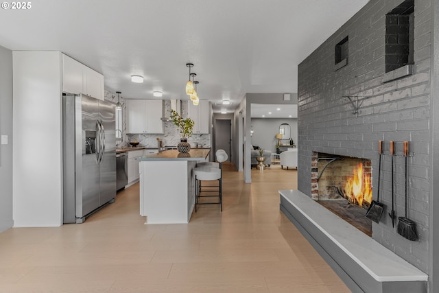 8318 SE Middle Way, Vancouver, WA 98664 - kitchen featuring appliances with stainless steel finishes, a brick fireplace, white cabinetry, a breakfast bar area, and a center island