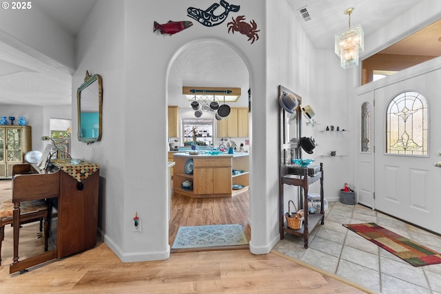 foyer with visible vents, baseboards, arched walkways, a high ceiling, and light wood-style floors