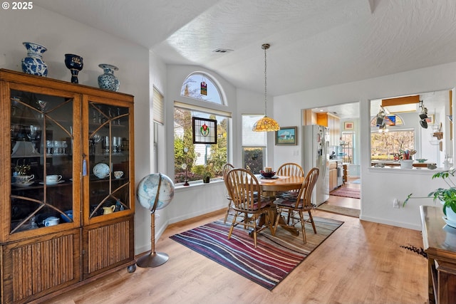 dining area with baseboards, vaulted ceiling, a textured ceiling, visible vents, and wood finished floors