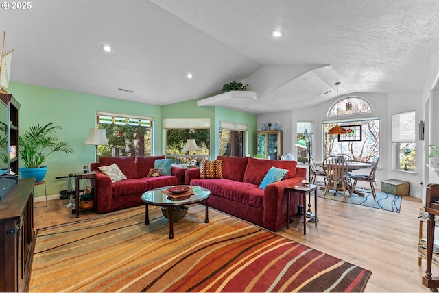 living room featuring visible vents, a wealth of natural light, vaulted ceiling, and wood finished floors
