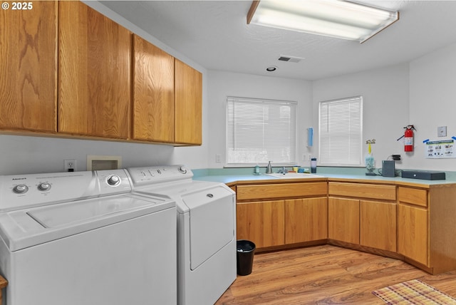 washroom with light wood-type flooring, visible vents, washer and clothes dryer, cabinet space, and a sink