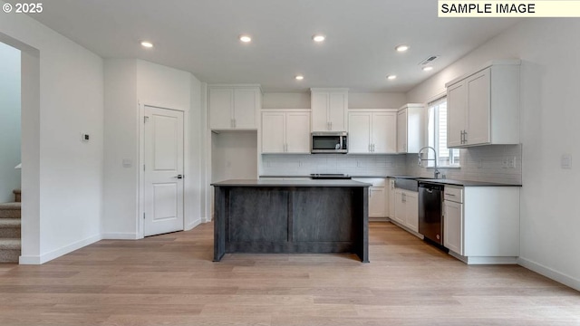 kitchen featuring light wood finished floors, a sink, decorative backsplash, stainless steel appliances, and white cabinets