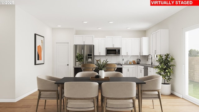 kitchen with light wood-type flooring, a sink, white cabinetry, appliances with stainless steel finishes, and decorative backsplash