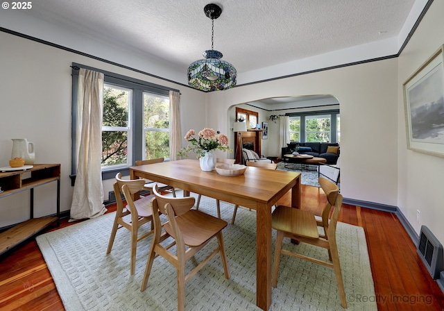 dining area featuring arched walkways, a textured ceiling, and wood finished floors
