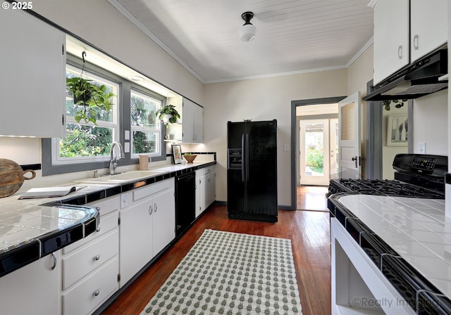 kitchen with black appliances, tile counters, under cabinet range hood, a sink, and ornamental molding