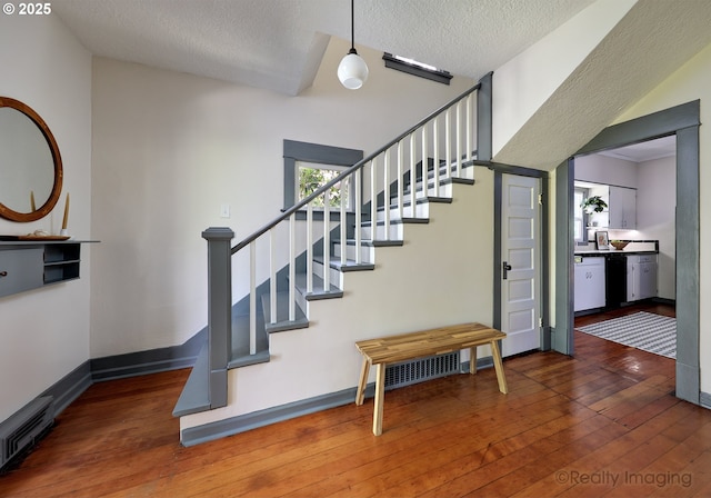 staircase featuring wood-type flooring, a textured ceiling, and baseboards