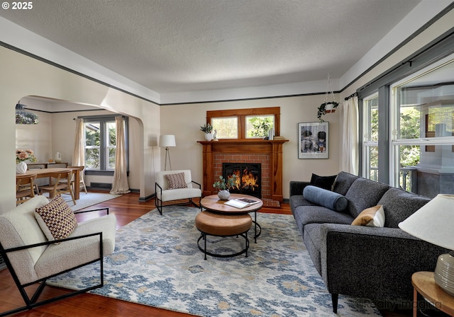 living room featuring arched walkways, wood finished floors, a fireplace, and a textured ceiling