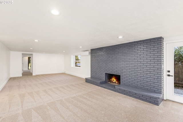 unfurnished living room featuring a fireplace, a wall mounted AC, and light carpet