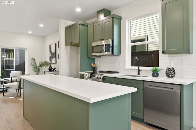 kitchen with sink, appliances with stainless steel finishes, green cabinetry, a kitchen island, and light wood-type flooring