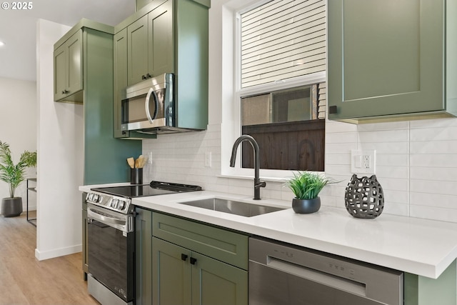 kitchen featuring sink, decorative backsplash, green cabinets, light hardwood / wood-style floors, and stainless steel appliances