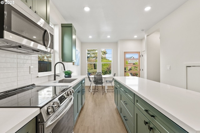 kitchen with sink, tasteful backsplash, green cabinetry, light wood-type flooring, and stainless steel appliances