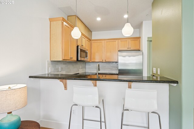 727 SE 33rd Pl Unit 21, Portland, OR 97214 - kitchen with appliances with stainless steel finishes, decorative backsplash, a peninsula, a breakfast bar area, and dark stone counters
