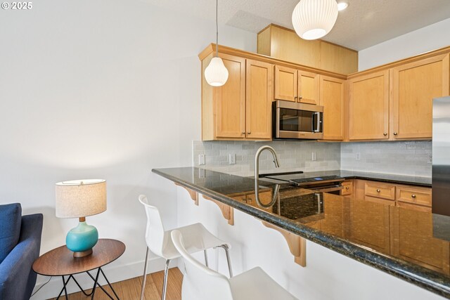 727 SE 33rd Pl Unit 21, Portland, OR 97214 - kitchen with stainless steel microwave, decorative backsplash, dark stone counters, a kitchen bar, and decorative light fixtures