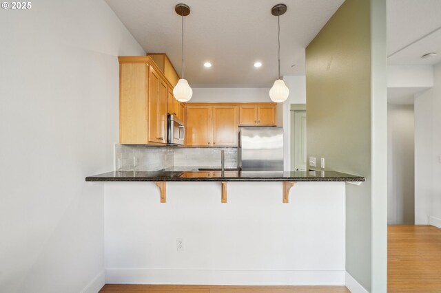 727 SE 33rd Pl Unit 21, Portland, OR 97214 - kitchen featuring appliances with stainless steel finishes, tasteful backsplash, dark stone counters, a breakfast bar area, and recessed lighting