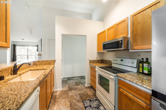 kitchen with stainless steel appliances, light stone counters, brown cabinetry, and a sink