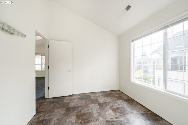 unfurnished room with lofted ceiling, stone finish flooring, and visible vents