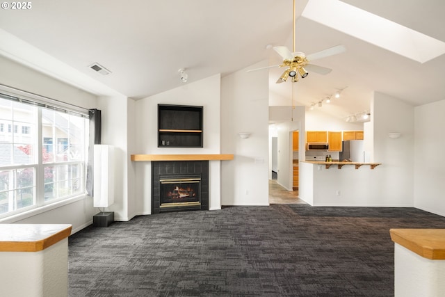 unfurnished living room with lofted ceiling, a tile fireplace, visible vents, a ceiling fan, and dark carpet