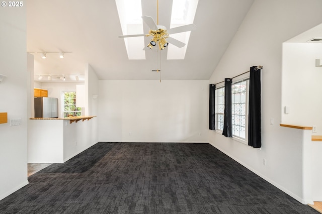 unfurnished living room with a healthy amount of sunlight, lofted ceiling with skylight, and dark colored carpet