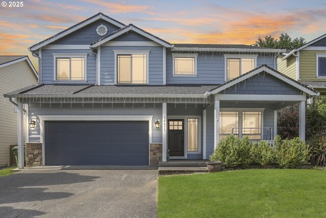 view of front of home featuring a porch, aphalt driveway, a front lawn, an attached garage, and stone siding