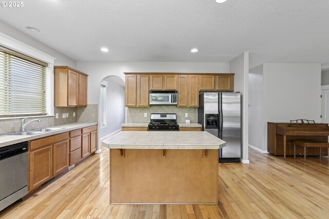 kitchen with a center island, arched walkways, light wood finished floors, and stainless steel appliances