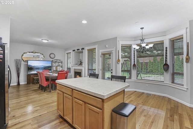 kitchen with a center island, light hardwood / wood-style flooring, a notable chandelier, stainless steel fridge, and decorative light fixtures