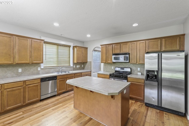 kitchen with brown cabinetry, appliances with stainless steel finishes, a center island, a sink, and light wood-style flooring