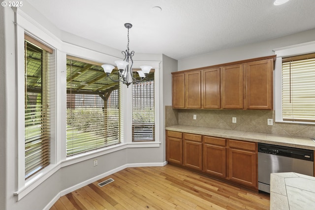 kitchen featuring tile countertops, visible vents, stainless steel dishwasher, light wood finished floors, and a chandelier