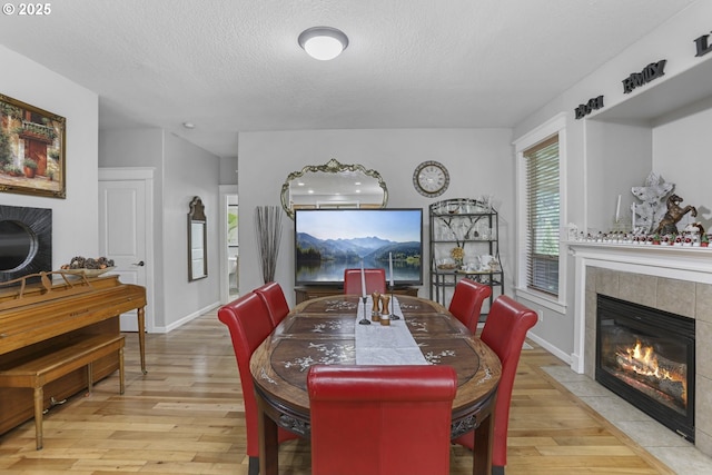 dining space featuring a textured ceiling, light wood-type flooring, and a tiled fireplace