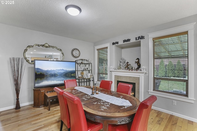 dining area with a tile fireplace, light hardwood / wood-style flooring, and a textured ceiling