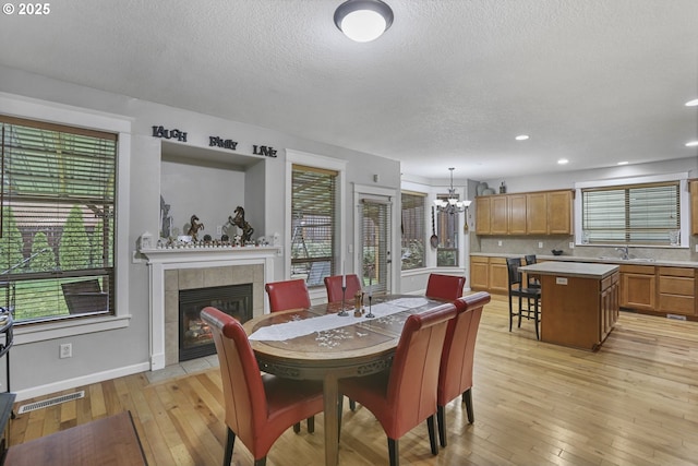 dining space featuring sink, an inviting chandelier, light hardwood / wood-style floors, a textured ceiling, and a fireplace